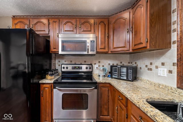 16226 Montrose Ln, Westfield, IN 46074 - kitchen featuring stainless steel appliances, a textured ceiling, brown cabinets, decorative backsplash, and light stone counters
