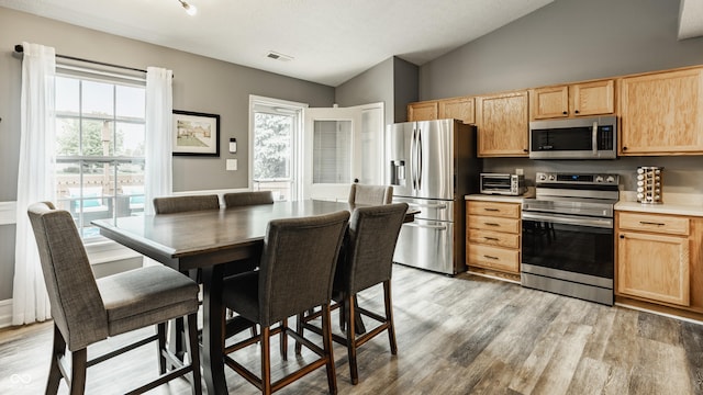 kitchen featuring stainless steel appliances, light brown cabinets, vaulted ceiling, and light wood-style flooring
