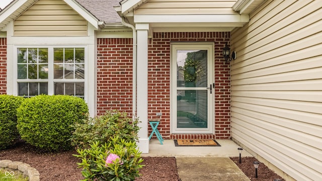 doorway to property with brick siding and roof with shingles