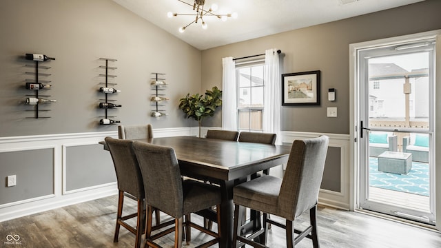 dining area featuring a chandelier, a decorative wall, light wood-style floors, lofted ceiling, and wainscoting