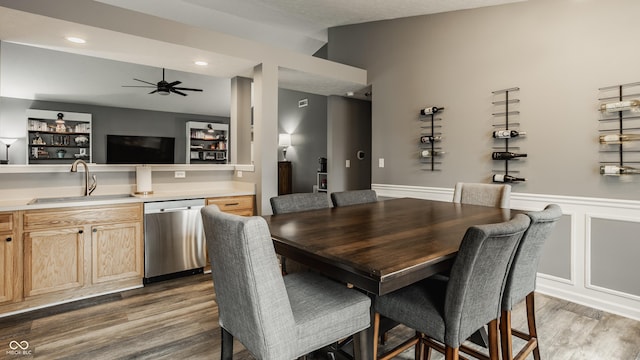 dining room with bar with sink, wood finished floors, a ceiling fan, wainscoting, and recessed lighting