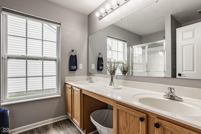 bathroom featuring wood finished floors, a shower stall, double vanity, and baseboards