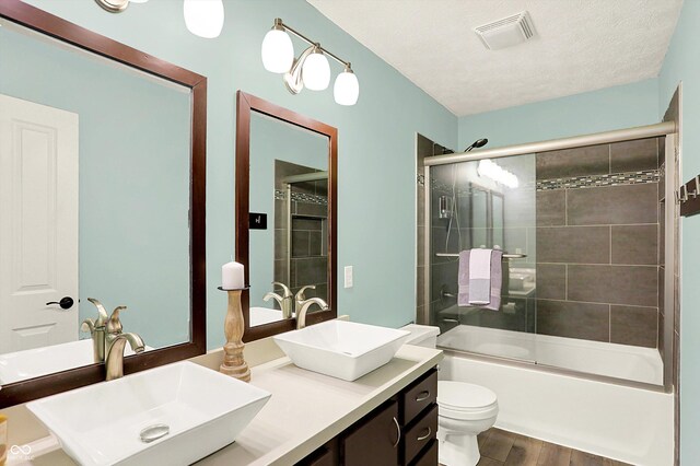 full bathroom featuring wood finished floors, toilet, bath / shower combo with glass door, and double vanity