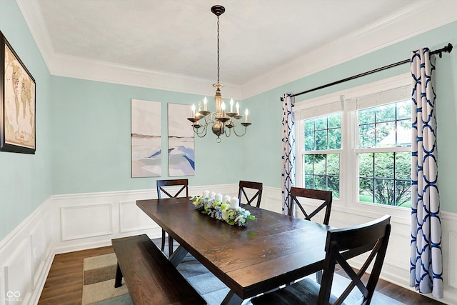 dining space with dark wood-type flooring, a chandelier, a decorative wall, crown molding, and a wainscoted wall