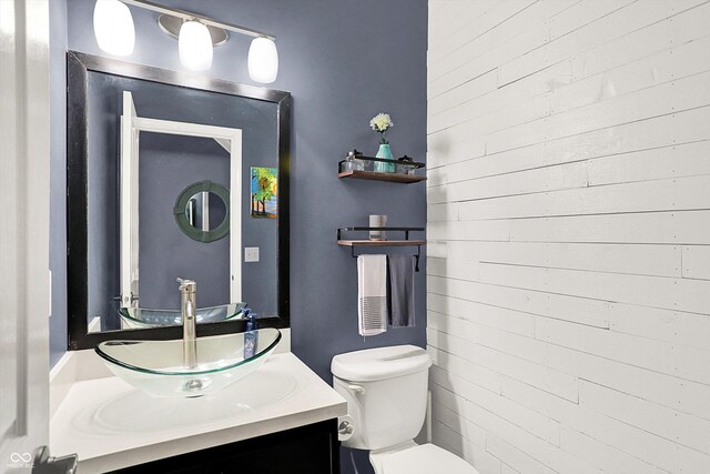 half bathroom featuring toilet, vanity, and wooden walls