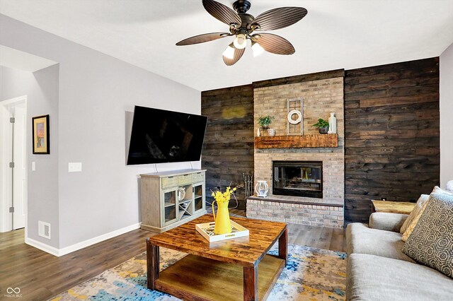 living room with a brick fireplace, a ceiling fan, baseboards, and wood finished floors