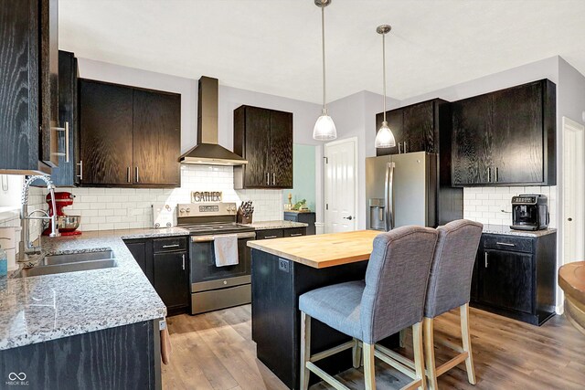kitchen with stainless steel appliances, wall chimney exhaust hood, a sink, tasteful backsplash, and light wood-style flooring