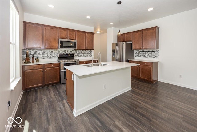 kitchen featuring appliances with stainless steel finishes, a sink, backsplash, dark wood-style flooring, and a kitchen island with sink