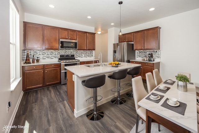 kitchen featuring appliances with stainless steel finishes, a sink, dark wood finished floors, decorative backsplash, and a kitchen breakfast bar