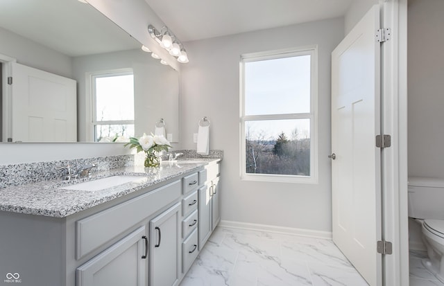 bathroom with toilet, healthy amount of natural light, marble look tiles, and double vanity