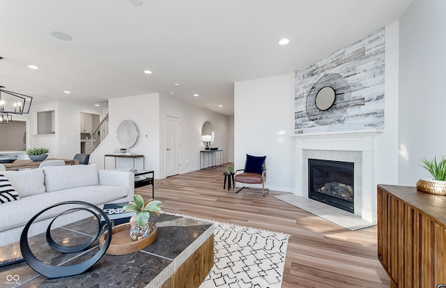 living area featuring light wood finished floors, a glass covered fireplace, recessed lighting, stairs, and a chandelier