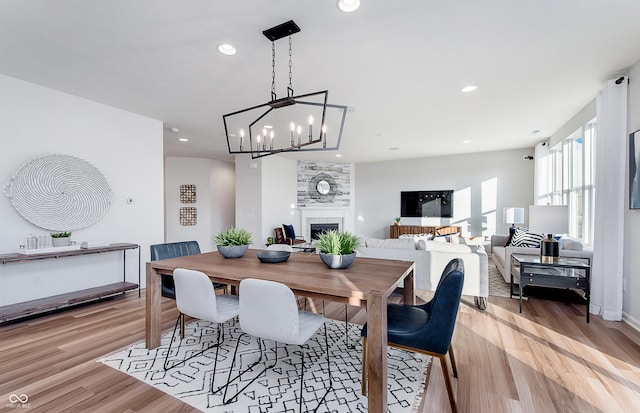 dining space featuring recessed lighting, light wood-style flooring, a tiled fireplace, and a chandelier