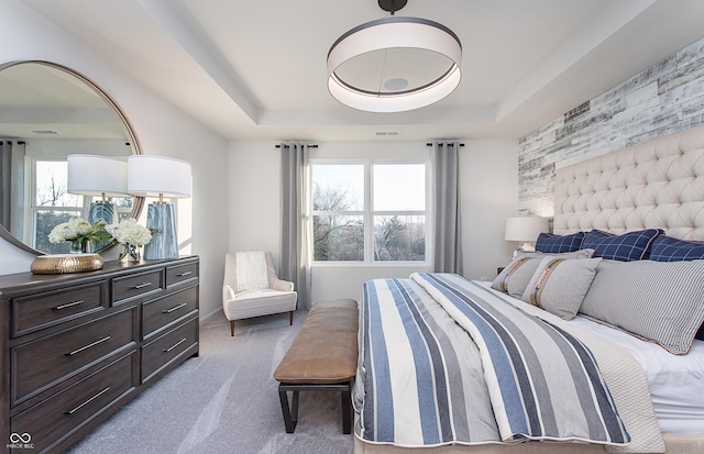 bedroom with a tray ceiling, carpet, and an accent wall