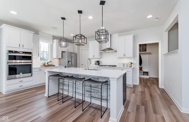 kitchen featuring stainless steel appliances, wall chimney exhaust hood, a sink, light wood-style flooring, and recessed lighting