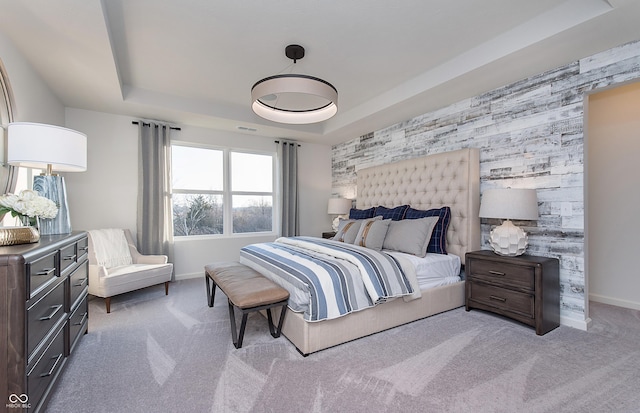 bedroom featuring an accent wall, a tray ceiling, light colored carpet, and baseboards