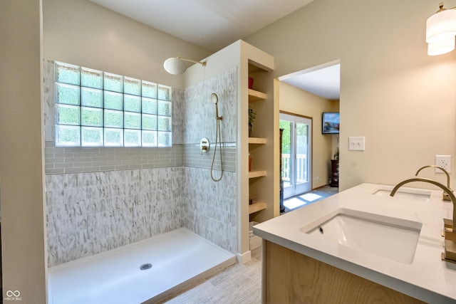 full bathroom with healthy amount of natural light, tiled shower, and double vanity