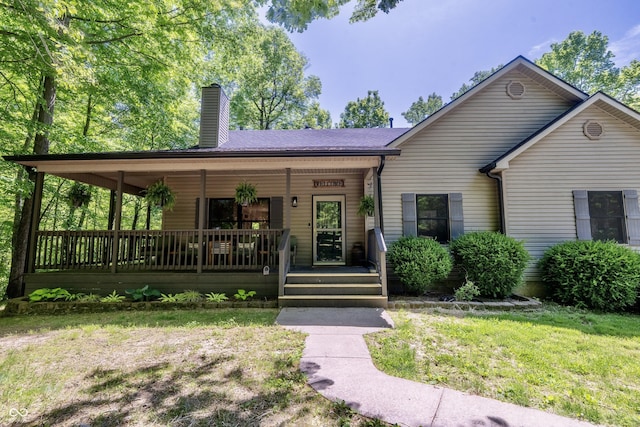 view of front of house featuring a porch, a chimney, and a front lawn