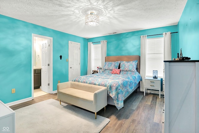 bedroom with wood finished floors, baseboards, a textured ceiling, and ensuite bath