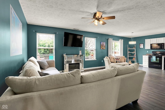 living room with dark wood-style flooring, ceiling fan, a textured ceiling, baseboards, and a glass covered fireplace
