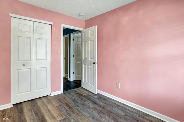 unfurnished bedroom featuring dark wood-type flooring, baseboards, a closet, and a textured ceiling