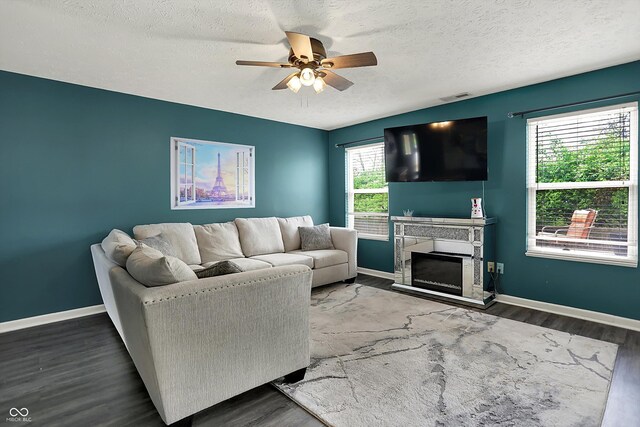 living room featuring a ceiling fan, wood finished floors, baseboards, a fireplace with raised hearth, and a textured ceiling