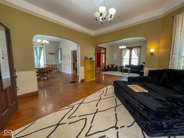 living room with a chandelier, arched walkways, wood finished floors, and wainscoting