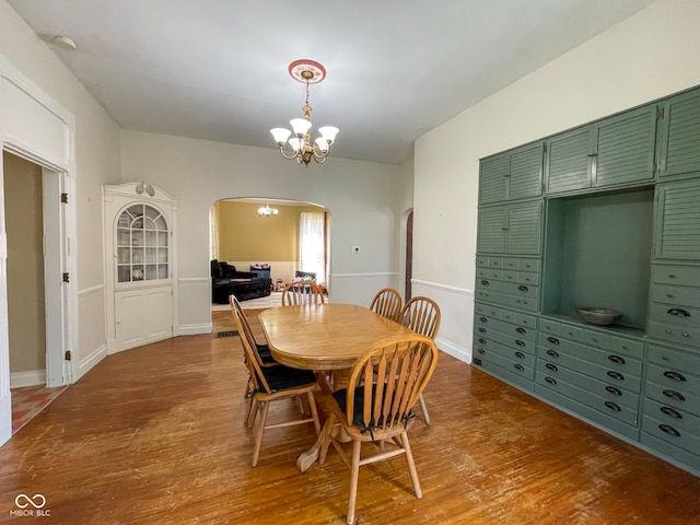 dining space with arched walkways, a chandelier, and wood finished floors