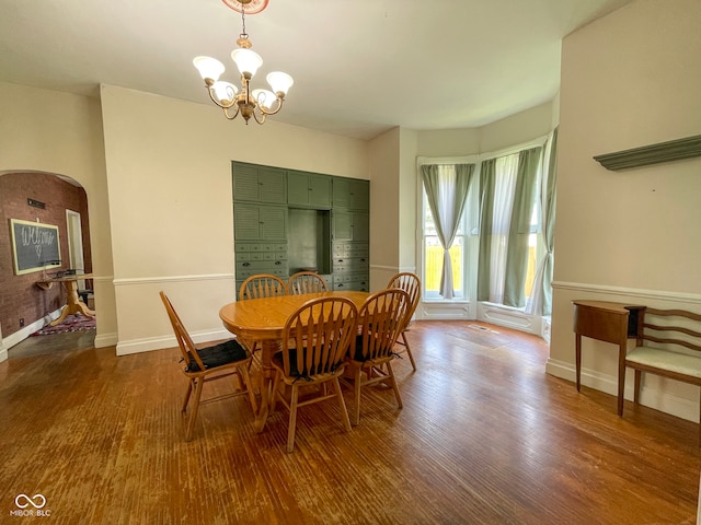 dining room with wood finished floors, arched walkways, a chandelier, and baseboards