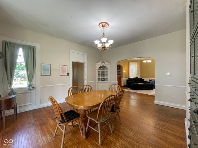 dining area with a chandelier, arched walkways, wood finished floors, and baseboards