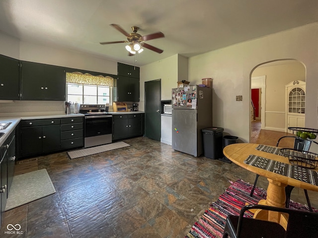 kitchen featuring stainless steel appliances, a ceiling fan, light countertops, and dark stone finish floors
