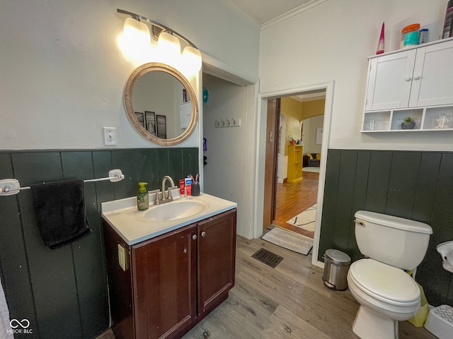 bathroom featuring wood finished floors, ornamental molding, wainscoting, vanity, and toilet