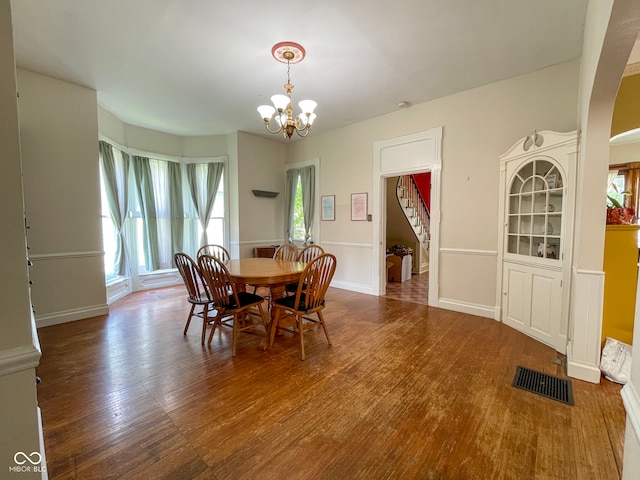 dining space featuring stairs, wood finished floors, a chandelier, and arched walkways