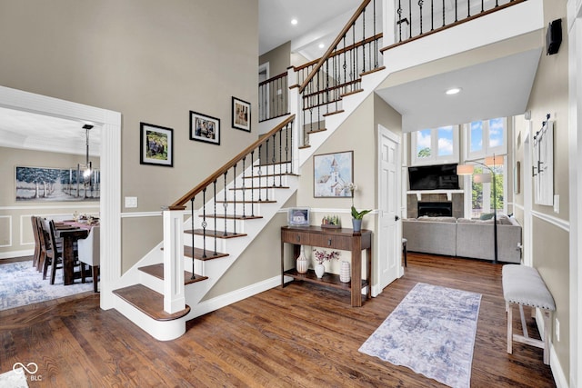 staircase featuring wood finished floors, a fireplace, a high ceiling, a chandelier, and recessed lighting