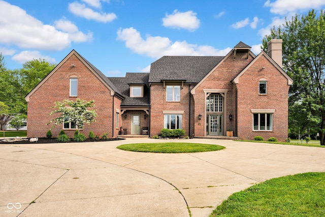 view of front of home featuring curved driveway, brick siding, roof with shingles, a chimney, and a front lawn