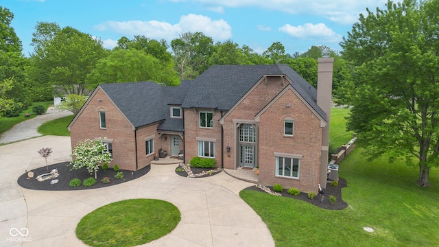 view of front of house with brick siding, a chimney, a front yard, and curved driveway