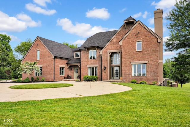 traditional-style home featuring a chimney, brick siding, a shingled roof, a front lawn, and a patio
