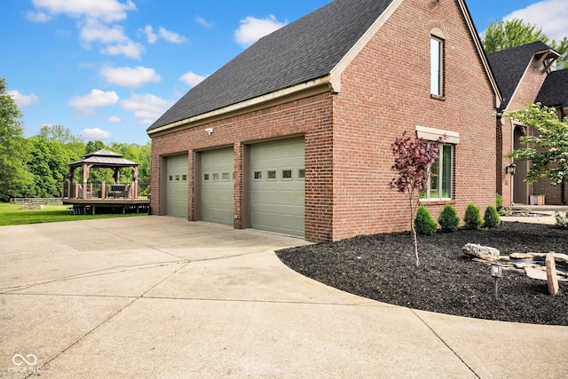 view of property exterior with a shingled roof, a gazebo, brick siding, a garage, and concrete driveway