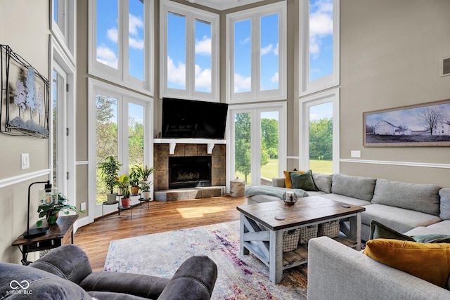 living room featuring a fireplace with raised hearth, wood finished floors, and a high ceiling