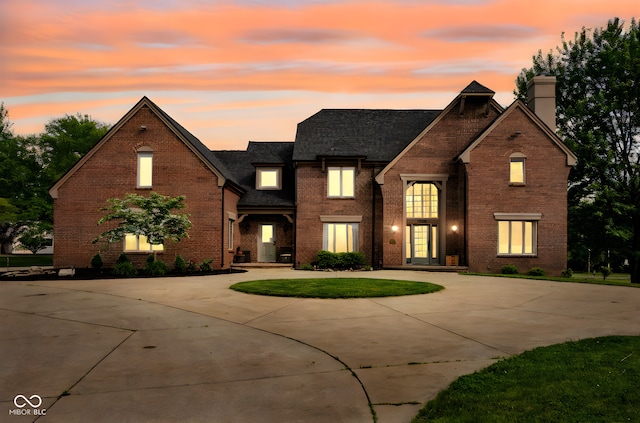 view of front of house with curved driveway, brick siding, a chimney, and roof with shingles