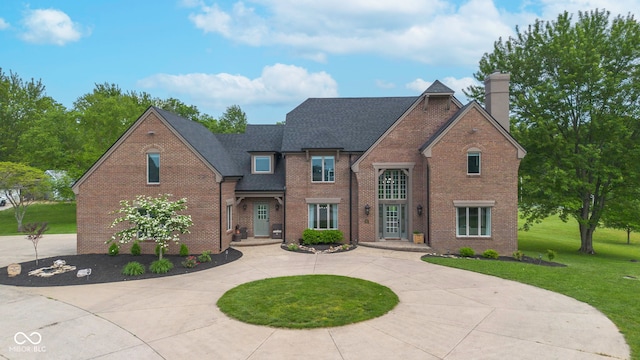 traditional home featuring curved driveway, brick siding, a front yard, a chimney, and a shingled roof