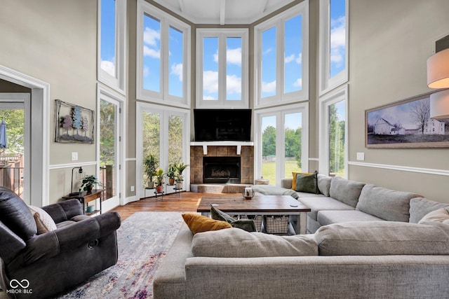 living area featuring a towering ceiling, a fireplace with raised hearth, and wood finished floors