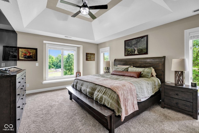 bedroom with a tray ceiling, light colored carpet, baseboards, and ceiling fan