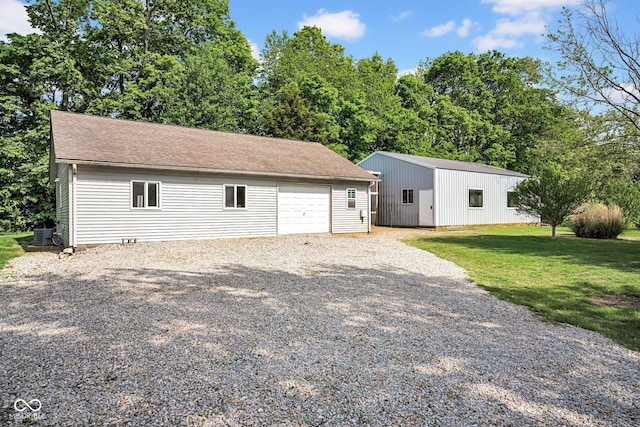 view of front of property with an outdoor structure, gravel driveway, a front yard, a detached garage, and central AC