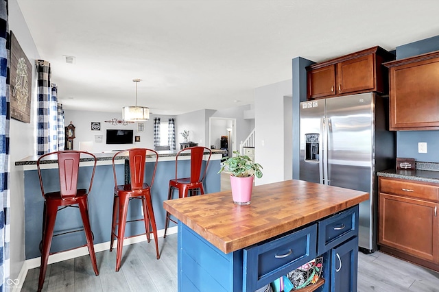 kitchen with stainless steel refrigerator with ice dispenser, light wood-type flooring, wooden counters, and a center island