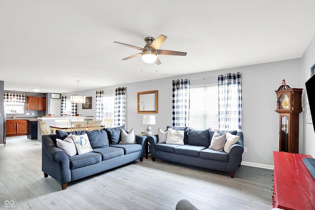 living area with healthy amount of natural light, ceiling fan, and light wood-style floors