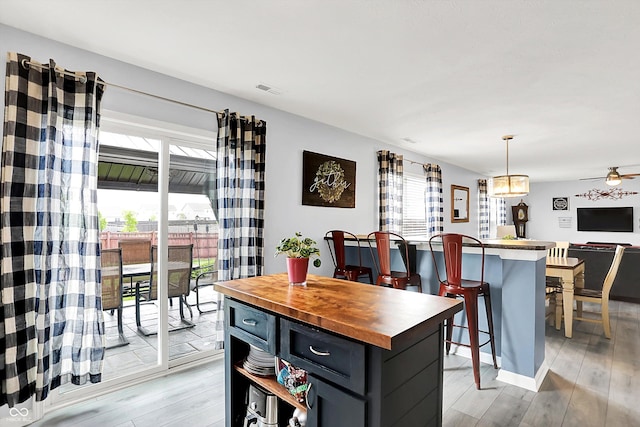 kitchen featuring butcher block countertops, light wood-type flooring, a kitchen island, open floor plan, and pendant lighting