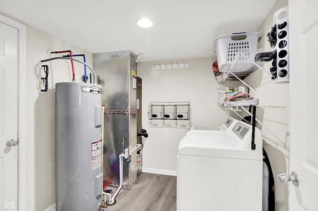 laundry area with electric water heater, washing machine and dryer, light wood-type flooring, baseboards, and heating unit