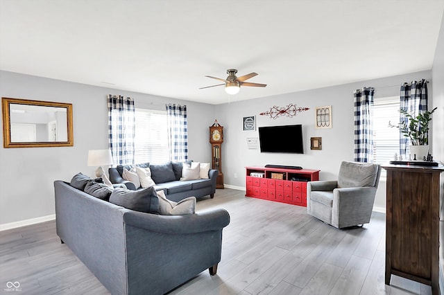 living room with ceiling fan, plenty of natural light, light wood-style floors, and baseboards