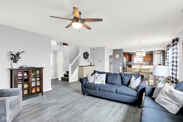 living room with stairway, light wood-style floors, ceiling fan, a chandelier, and baseboards