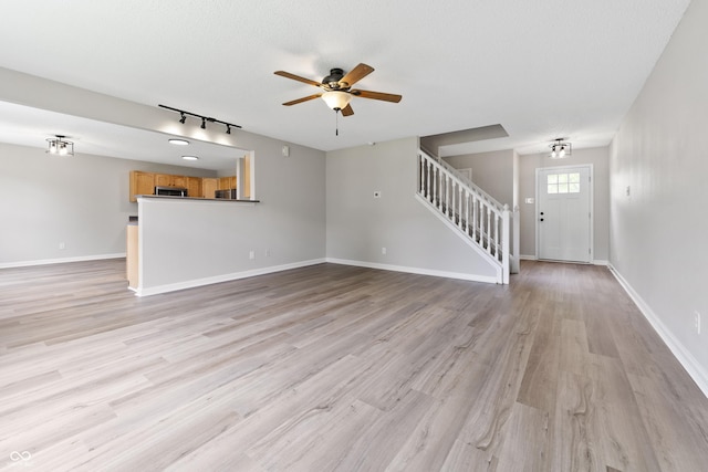 unfurnished living room featuring stairway, a ceiling fan, light wood-style flooring, and rail lighting